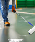 Worker using 9 Inch Spiked Roller For Self Leveling Screeds And Epoxy Floors Pro Grade Bubble Removal Tool with blue handle