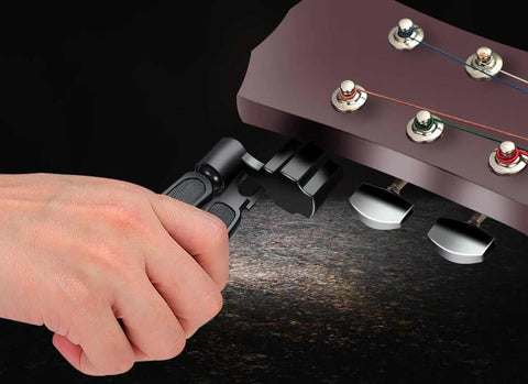 Guitar string winder cutter pin puller 3-in-1 tool with black handles being used on a guitar headstock