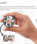 Hand holding a grey and white ceramic cabinet knob with floral design, part of the Assorted Ceramic Cabinet Knobs Set Of 12 In Grey And White With Vintage Old School Charm For Cupboard Doors And Drawers Handmade Look Chrome Hardware Finish Perfect For Kitchen Cabinets And DIY Furniture Renovations.