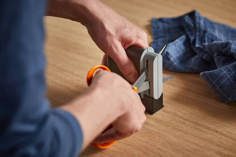 "Clip Sharp Scissors Sharpener For All Scissors, Quick No Fuss Sharpening, Extends Shears Life in action on a wooden table."
