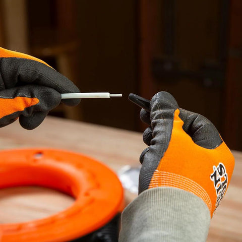 Klein Tools 56025 non-conductive fish tape repair kit held by gloved hands; white plastic rod, orange coil nearby.