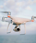 White quadcopter drone flying in the sky with ocean background.