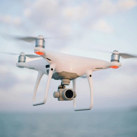White quadcopter drone flying in the sky with ocean background.