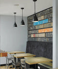 Three modern black pendant lights hanging over wooden tables in a rustic styled dining area with graphic wall paneling.