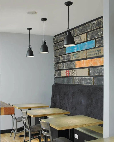 Three modern black pendant lights hanging over wooden tables in a rustic styled dining area with graphic wall paneling.