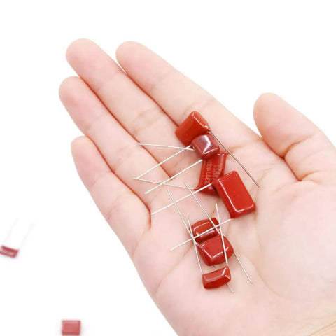 Hand holding red capacitors from 150 Piece CBB Metallized Polypropylene Film Capacitor Kit 400V-630V Range 10nF To 68nF 0.01uF To 0.068uF ±5% Tolerance Red Radial Lead Assortment For DIY Electronics Projects