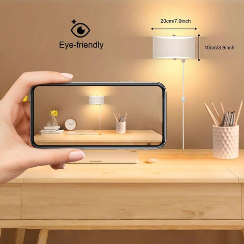 Hand holding phone capturing 12W Plug-In LED Wall Sconce With Dimmable Up-Down Lighting for cozy warm white glow in bedroom.