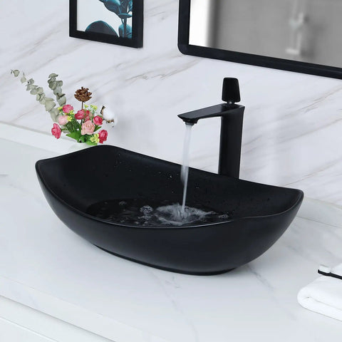 Black ceramic vessel sink with faucet in a modern bathroom setting with floral decoration on the white vanity countertop.