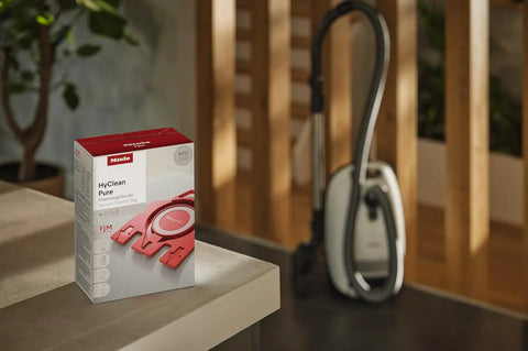 Box of AirClean Dust Bags Type FJM HyClean for vacuum cleaners beside a Miele vacuum cleaner in a home setting.
