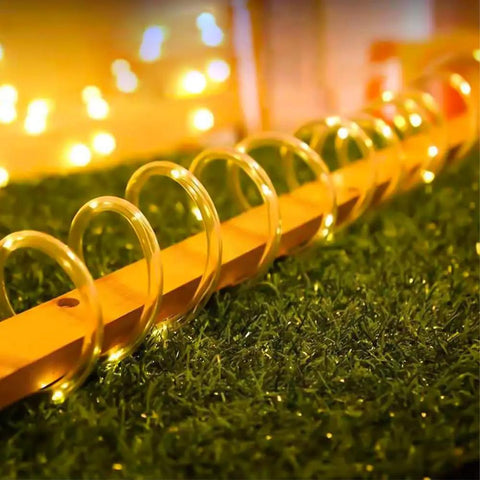 33ft Solar Rope Lights With 100 LEDs, 8 Modes, IP65 Waterproof Tube Lights glowing warmly on outdoor grass surface