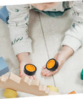 Child playing with two orange rubber tires from 10 Pcs DIY Car Wheels For Kids Toy Replacement Small Rubber Tires With 0.08 In Axle Hole For Model Cars And Science Projects Durable Craft Accessories For Hobbyists And Classroom Projects
