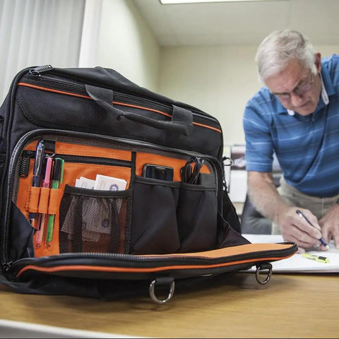 Tradesman Pro Tech Tool Bag With Laptop Pocket And 22 Pockets, open showing orange interior with tools, man writing at desk