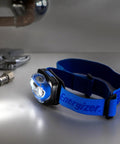 Vision LED Headlamp 200 Lumen 4 Pack With 12 AAA Batteries Included, hands-free, blue adjustable strap on a workbench.