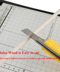 Cutting Top Shelf Unfinished Balsa Wood Dowels 12 Pack with a utility knife on a grid cutting mat.