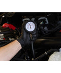 Mityvac MV5530 compression tester gauge held by a gloved hand in a car engine bay.