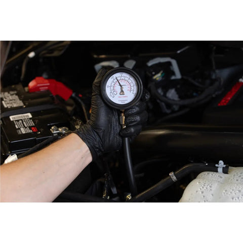 Mityvac MV5530 compression tester gauge held by a gloved hand in a car engine bay.
