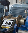 Technician using monitoring equipment for machine calibration in an industrial setting with large machinery in the background.
