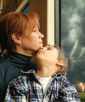 Woman and child looking out window during storm, representing safety and awareness concept with WR120B NOAA Emergency Weather Alert Radio.