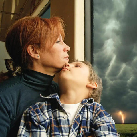 Woman and child looking out window during storm, representing safety and awareness concept with WR120B NOAA Emergency Weather Alert Radio.