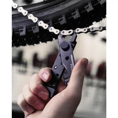 Hand using All In One Bike Chain Tool With Quick Link Pliers, Chain Breaker, Magnetic Link Storage, Rotor Aligner, Valve Core Wrench And Bottle Opener For Trailside Repairs, Durable Aluminum Multi Tool For On The Go Fixes on bike chain