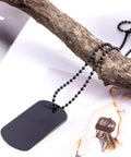Black dog tag pendant necklace on black bead chain draped over a branch with a fashion magazine background.