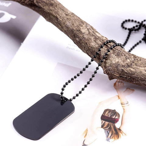 Black dog tag pendant necklace on black bead chain draped over a branch with a fashion magazine background.
