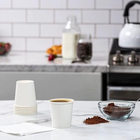 Stack of 3 oz white paper cups with filled cup on kitchen counter, designed for espresso, tea or mouthwash. Set of 600 for hot or cold drinks.