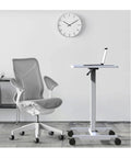 Fully Adjustable Rolling Laptop Stand With Rugged Aluminum Frame Convertible Standing Desk Tray next to modern office chair.