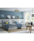 Calm coastal bedroom with twin beds, light blue walls, and a round rattan dining table near window. Pendant light overhead.