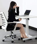 Slick Electric Height Adjustable Lectern With Smooth Roll Wheels For Boardroom Church Or Lecture Hall Speaking Ergonomic Mobile Standing Podium Designed For All Day Grind And Zero Sweat Operation in use with user at a desk.