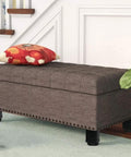 Tufted grey storage bench with black legs beside staircase, decorative red pillow on top