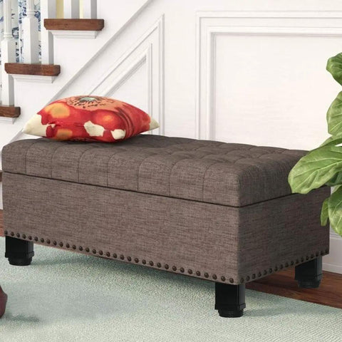 Tufted grey storage bench with black legs beside staircase, decorative red pillow on top