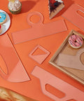High Density Acrylic Charcuterie Board Templates Six Piece Router Stencil Set With Grippy Handles on orange table with pastries.