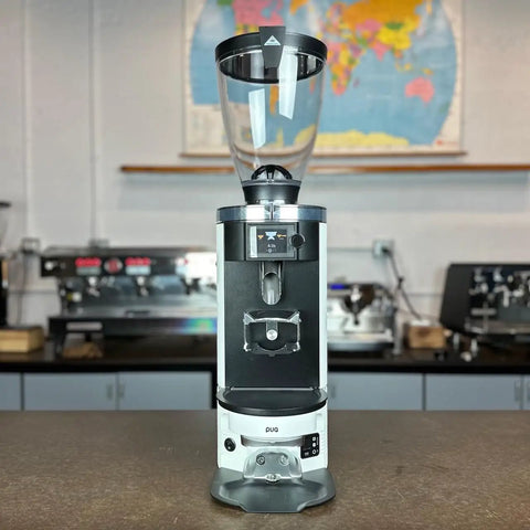 Automatic Espresso Coffee Tamper Built To Deliver Dead On Pulls With Calibrated Pressure And Adjustable Profiles That Fit Like A Glove On Mahlkonig E65 Grinders For Effortless Brews, grinding coffee with a modern black and white design.