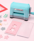 Portable Die Cutting And Embossing Machine For Card Making And Scrapbooking No Fuss Mini Cutter For Paper Crafting Easy Manual Operation Works With Dies And Folders Up To 3 Inches Wide shown with flower die cutouts on pink surface