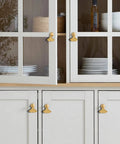 Six Piece Golden Ginkgo Leaf Cabinet Knobs on gray cabinets with glass doors, displaying plates and jars inside.
