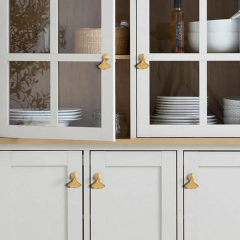 Six Piece Golden Ginkgo Leaf Cabinet Knobs on gray cabinets with glass doors, displaying plates and jars inside.