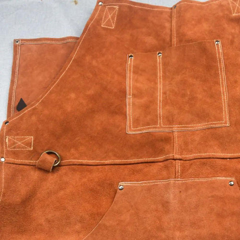 Close-up of brown leather welding apron with flame resistant shield and six tool pockets, built to last.