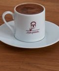 White cup of Authentic Turkish Coffee From Mehmet Efendi Tradition, 100 Percent Arabica Ground Extra Fine For Cezve on saucer.