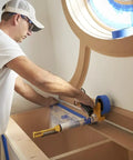 Person using Pro Grade Masking Film Kit With Static Cling 8 Rolls Of 48 In By 180 Ft Each Keeps Film In Place on cabinet edge.