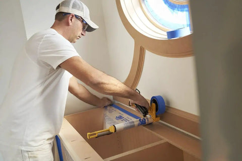 Person using Pro Grade Masking Film Kit With Static Cling 8 Rolls Of 48 In By 180 Ft Each Keeps Film In Place on cabinet edge.