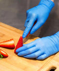 Person slicing strawberries while wearing Top Notch Disposable Vinyl Exam Gloves In Steel Blue, Cast At Four Mil Thick For Daily Grind Demands, Zero Latex And Powder, Sharp For Medical Visits Or Quick Kitchen Washes, One Hundred Pack Boxes Ensure Legit Finger Comfort On Every Use.