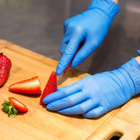 Person slicing strawberries while wearing Top Notch Disposable Vinyl Exam Gloves In Steel Blue, Cast At Four Mil Thick For Daily Grind Demands, Zero Latex And Powder, Sharp For Medical Visits Or Quick Kitchen Washes, One Hundred Pack Boxes Ensure Legit Finger Comfort On Every Use.