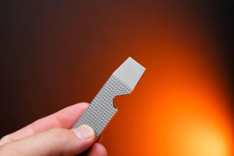 Ultra Slim Pry Bar Keychain Tool Pocket Titanium Multitool for Everyday Carry held against orange background