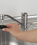 Hand using a faucet sprayer attachment with running water over a stainless steel sink.