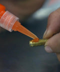 Permatex 25210 orange threadlocker, 10 ml, applied to a threaded bolt (close-up)