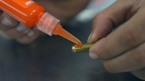 Permatex 25210 orange threadlocker, 10 ml, applied to a threaded bolt (close-up)