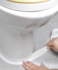 Applying the Waterproof Self Adhesive Caulking Tape For Bathrooms And Kitchens Peel And Stick Sealant Strip around a toilet base.
