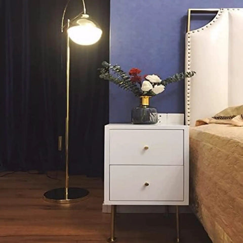 White nightstand with gold drawer knobs and Four Pack Adjustable Solid Brass Furniture Legs For Sofa, Cabinet, Coffee Table, TV Stand, Bathroom Cabinet And More - Gold Finish 250mm 9.84in Heavy Duty Metal Sofa Support Legs, next to a floor lamp and bed in a bedroom