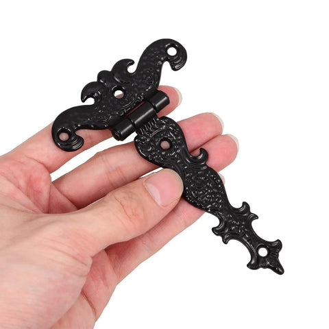 Hand holding vintage style black zinc alloy tee door hinge, slip joint lift off, for cabinets and sheds, 2 pack shown.